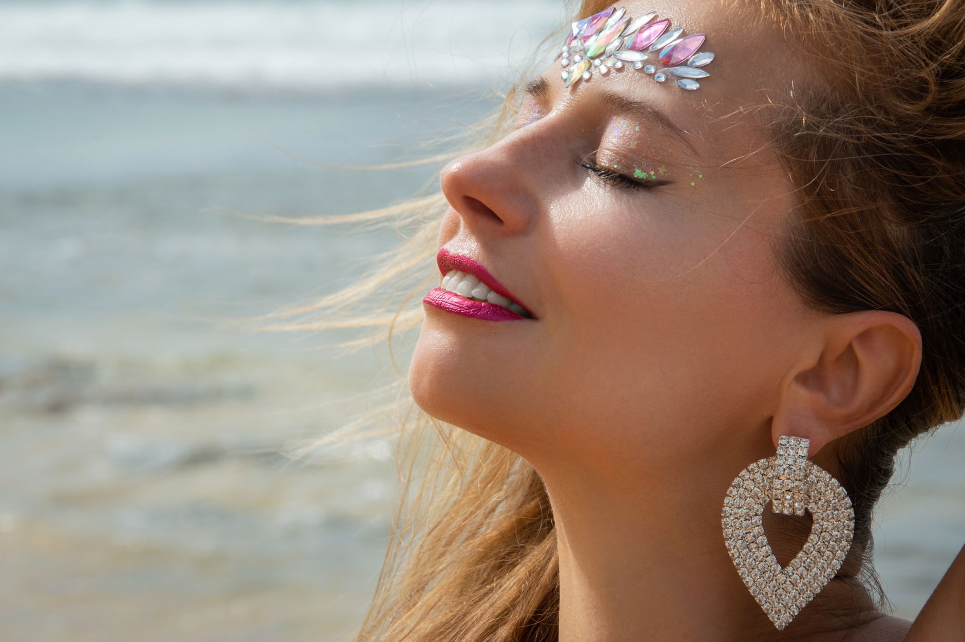 Close-up of hands applying cream bronzer with a makeup brush near a sunlit window with a beach towel nearby